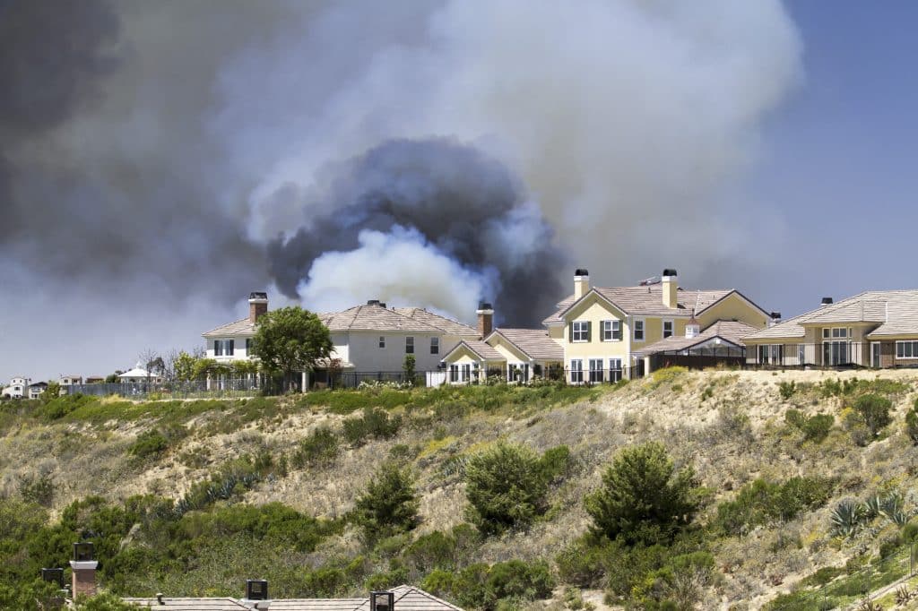 Smoke from a brush fire rising behind hillside homes